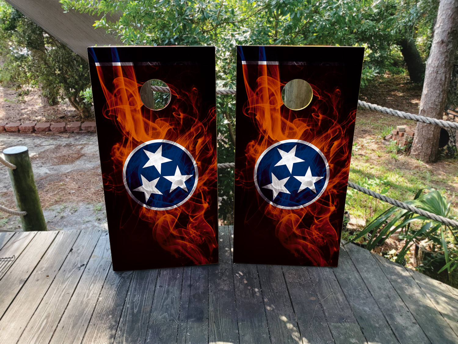 Two cornhole boards with flame design and Tennessee flag logo on a wooden surface outdoors.