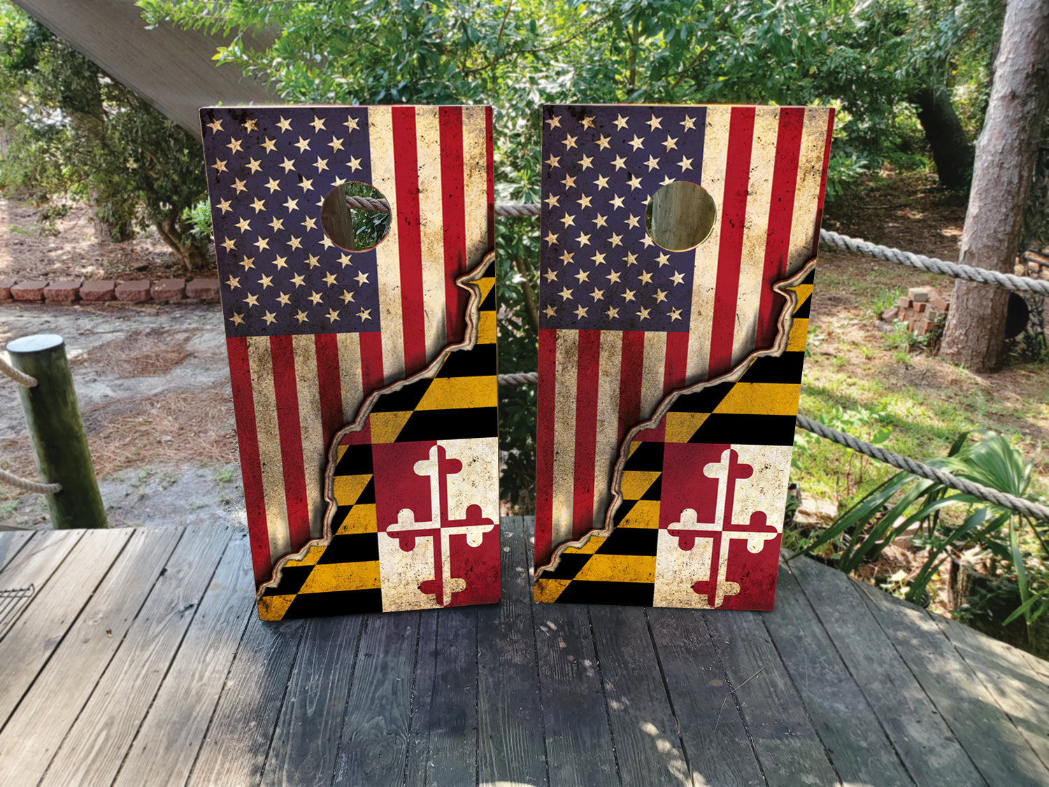 Two cornhole boards with American and Maryland flags on a wooden surface outdoors.