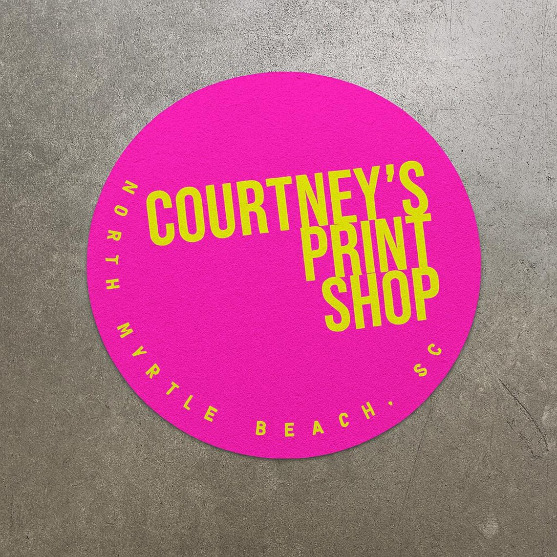 Round pink sticker with yellow text 'Courtney's Print Shop' on a gray background